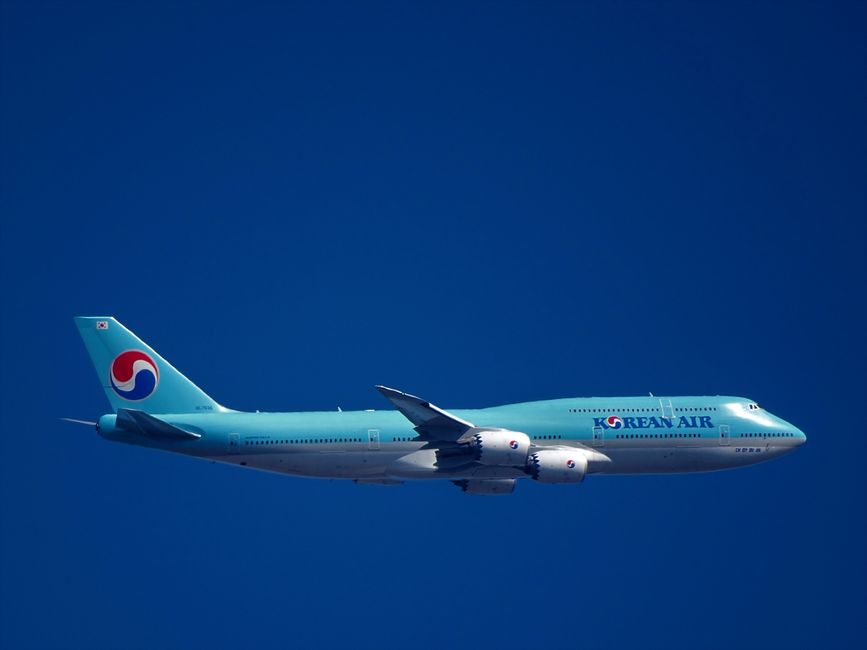 A Korean Air Boeing 747 flies through a clear blue sky, depicting air travel and aviation.