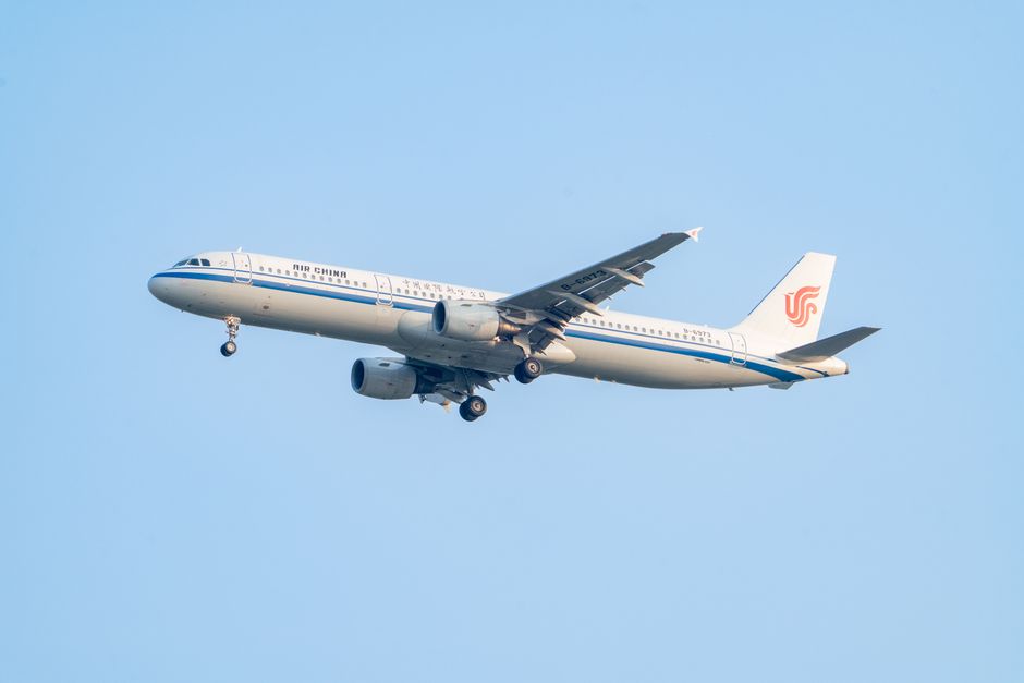 Air China Airbus A321 soaring mid-flight against a clear blue sky, showcasing its sleek design.