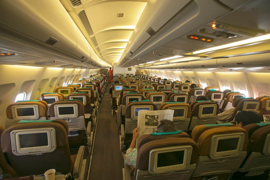 View of an airplane's cabin interior with passengers seated, highlighting in-flight entertainment.