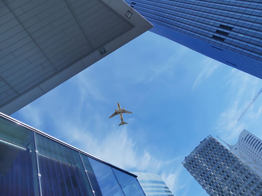 Low angle view of an airplane flying over modern skyscrapers against a blue sky in Vienna.