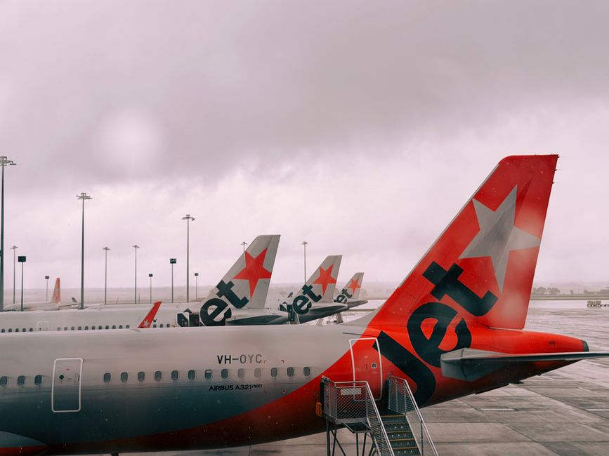 Jetstar Airbus A321neo airplanes lined at Melbourne Airport under a cloudy sky.