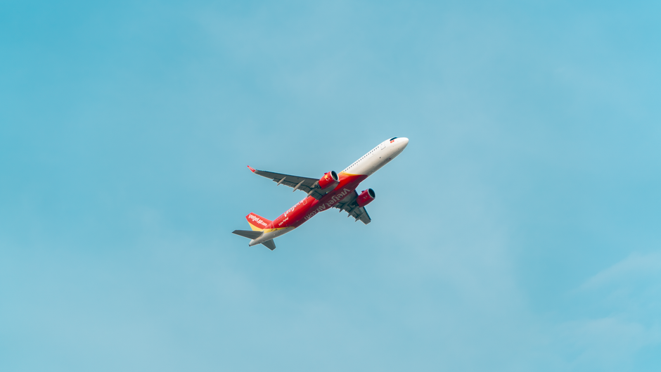 Commercial airplane with red livery flying high in a clear blue sky.