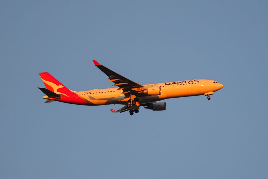A vibrant Qantas passenger plane in flight against a clear blue sky during sunset.