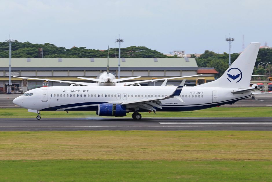 A commercial airplane from Alliance Jet lands on a runway at an airport during the day.