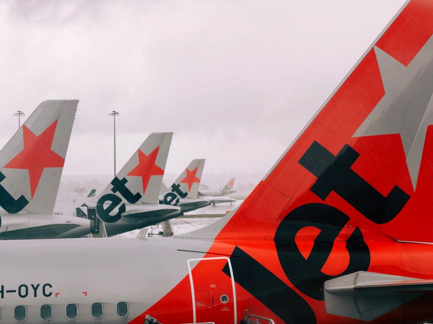 Jetstar planes lined up at Melbourne Airport on a cloudy day, showcasing airline fleet.